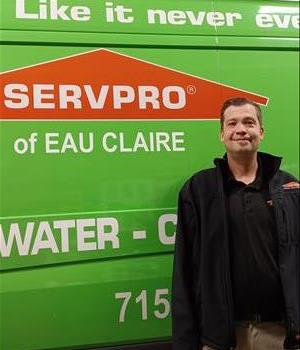 Tall male with smile standing in front of a green SERVPRO van.