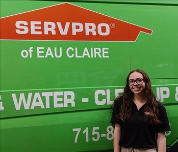 young girl with glasses standing in front of a green SERVPRO van.